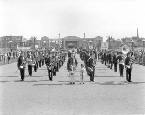 Members of the employees' shop bands of the Denver & Rio Grande Western Railroad pose in columns, with instruments in center of Civic Center, Denver, Colorado. A man with a trophy cup and a boy with a baton stand. (circa 1923-1930)
